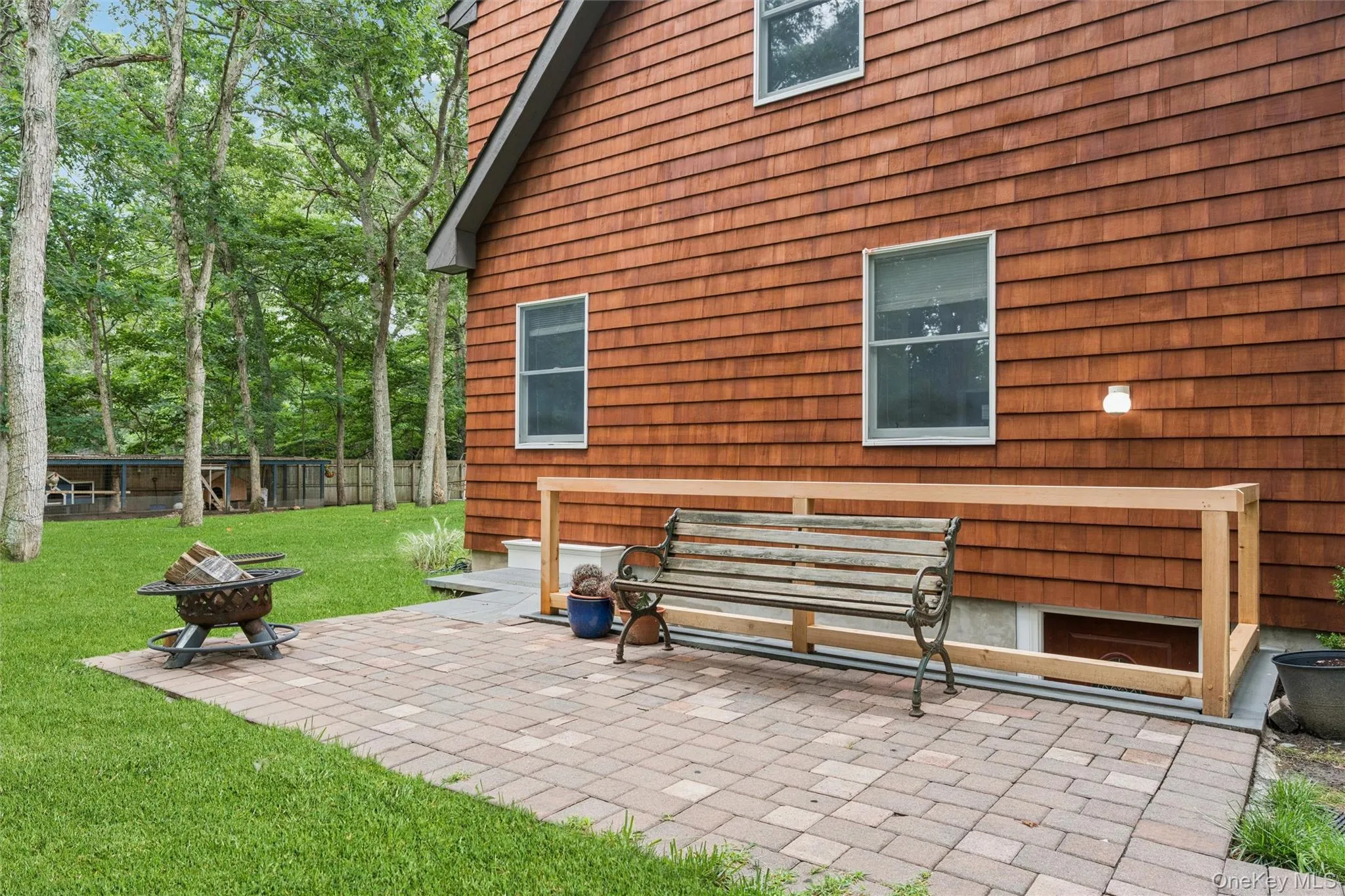 Cedar shake siding, paver patio, established lawn, mature trees, and a wooden railing Cedar shake siding, paver patio, established lawn, mature trees, and a wooden railing