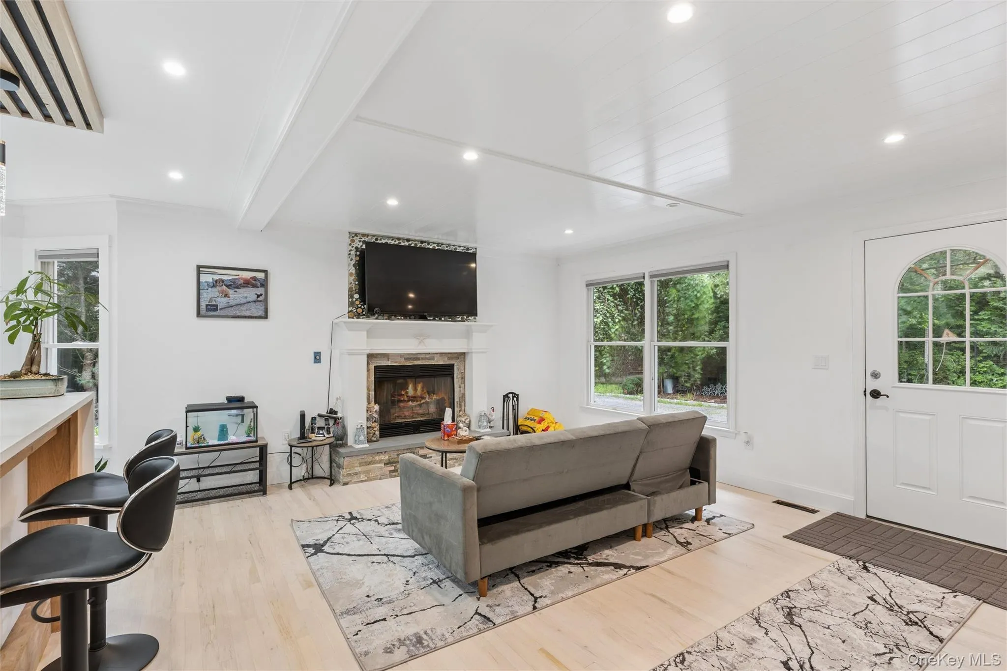 Vaulted ceiling with exposed beams, recessed lighting, wood-finish flooring, stone fireplace, and a white paneled entry door with an arched window Vaulted ceiling with exposed beams, recessed lighting, wood-finish flooring, stone fireplace, and a white paneled entry door with an arched window