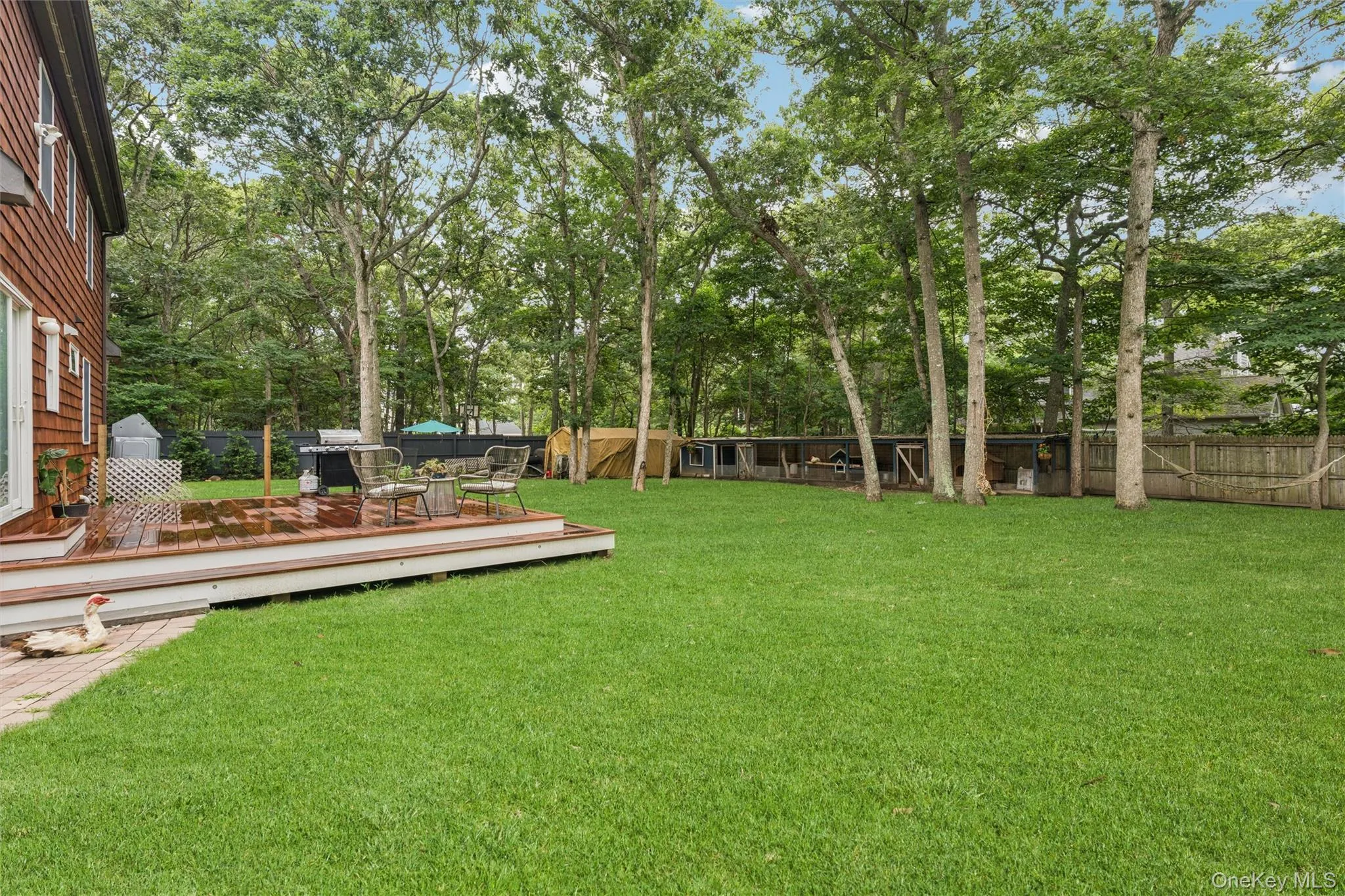Expansive green lawn with mature trees, a multi-level wood-finish deck, and wood siding on the exterior Expansive green lawn with mature trees, a multi-level wood-finish deck, and wood siding on the exterior