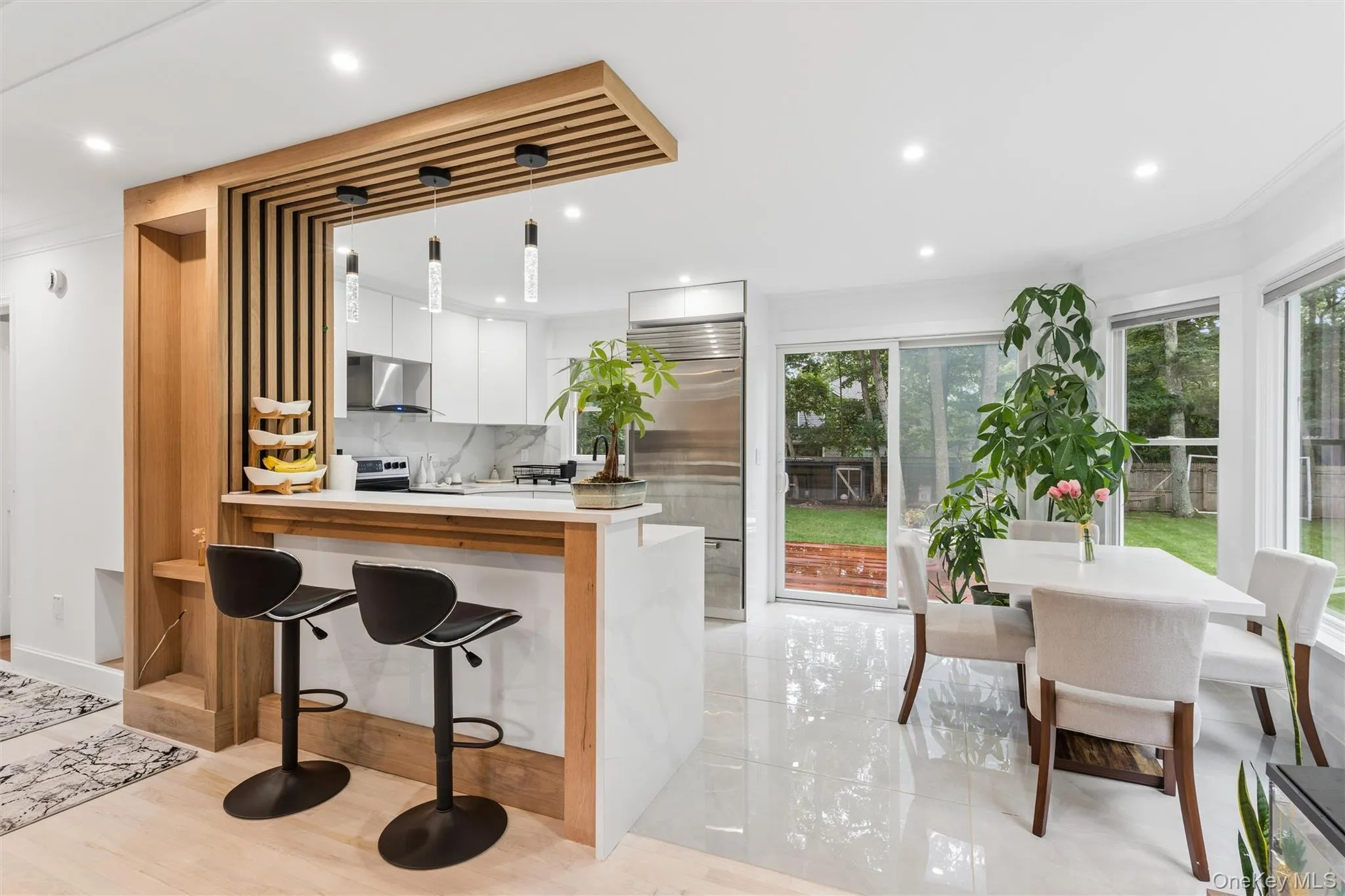 Modern kitchen featuring white cabinetry, stainless steel appliances, a breakfast bar with pendant lighting, a sliding glass door, and a dining area with bay windows Modern kitchen featuring white cabinetry, stainless steel appliances, a breakfast bar with pendant lighting, a sliding glass door, and a dining area with bay windows