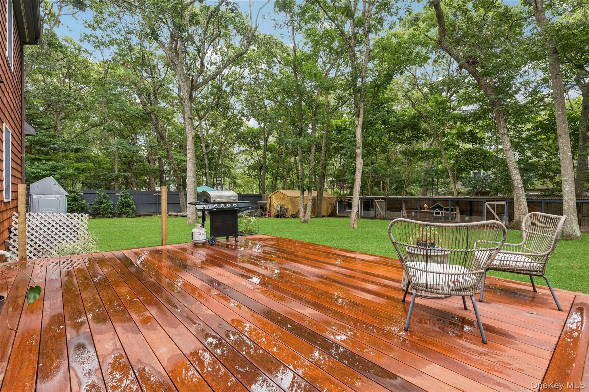 Expansive wooden deck with natural wood siding, leading to a manicured lawn framed by mature trees Expansive wooden deck with natural wood siding, leading to a manicured lawn framed by mature trees