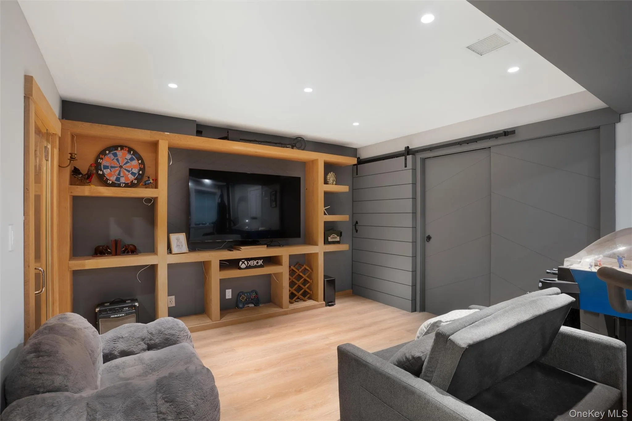 Recessed lighting, wood-finish flooring, built-in media console with shelving, and sliding barn doors with matte black hardware Recessed lighting, wood-finish flooring, built-in media console with shelving, and sliding barn doors with matte black hardware