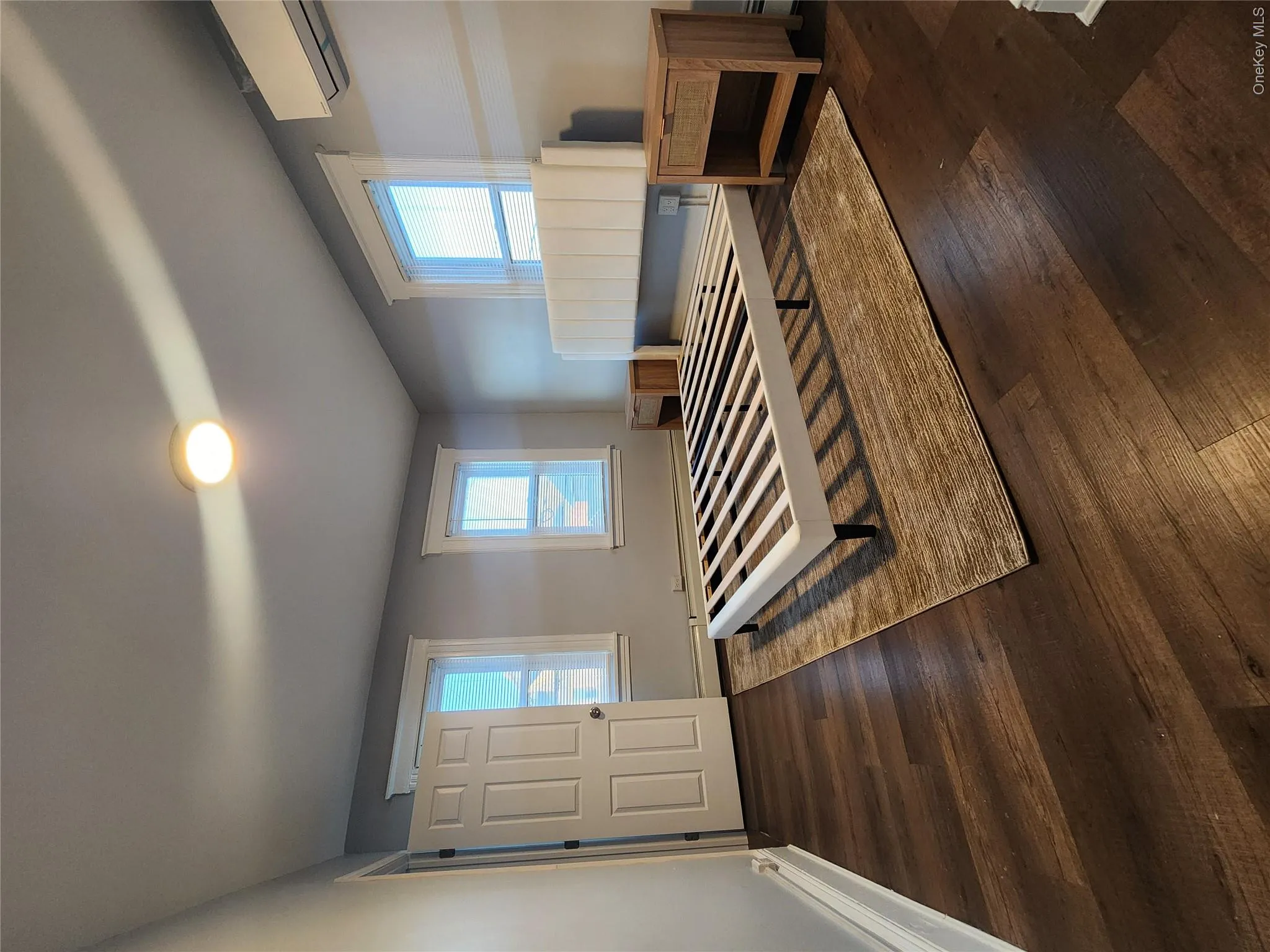 Bedroom featuring wood finished floors, an AC wall unit, multiple windows, and a baseboard heating unit Bedroom featuring wood finished floors, an AC wall unit, multiple windows, and a baseboard heating unit