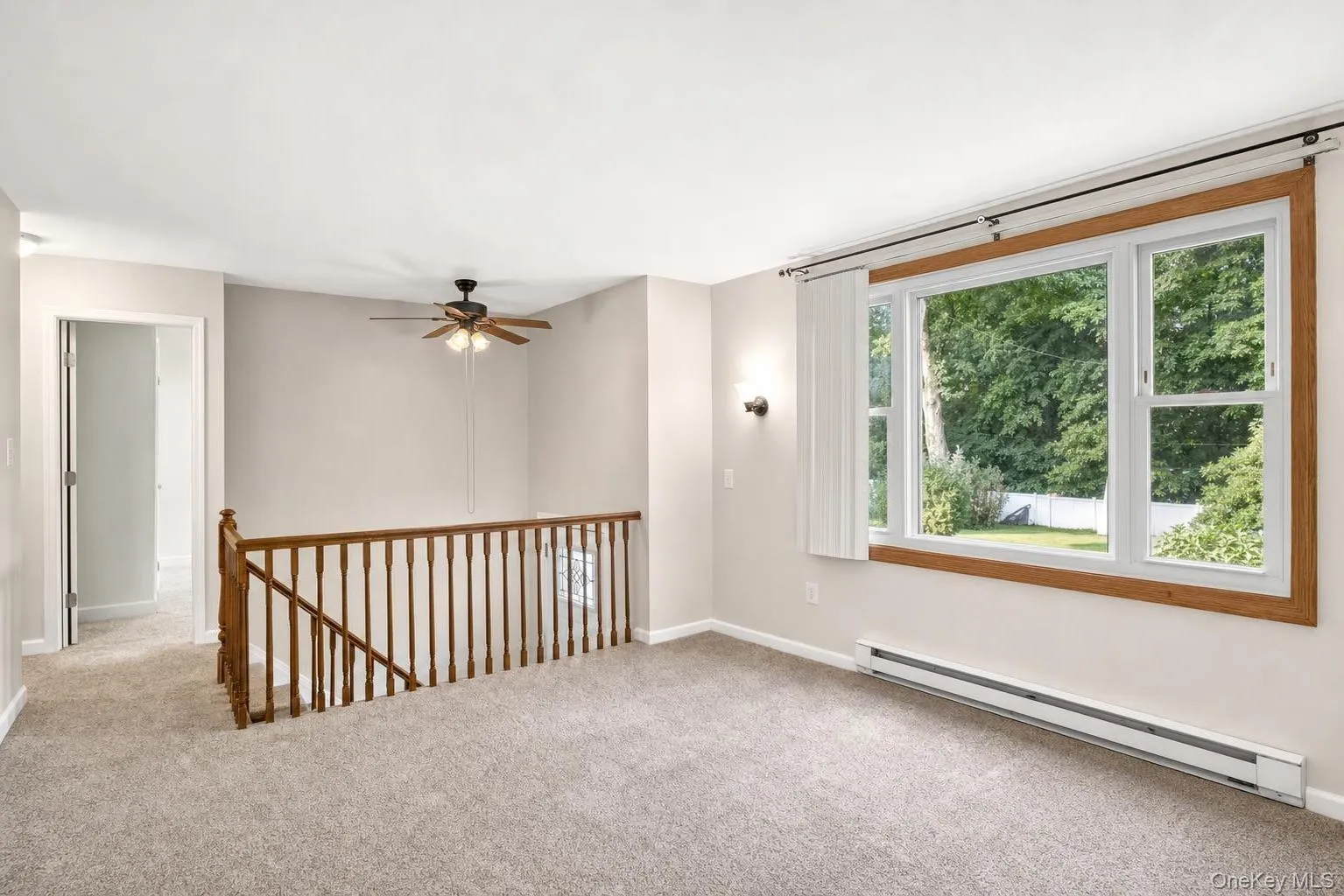 Carpeted interior with a large window, wooden railing, and a ceiling fan Carpeted interior with a large window, wooden railing, and a ceiling fan