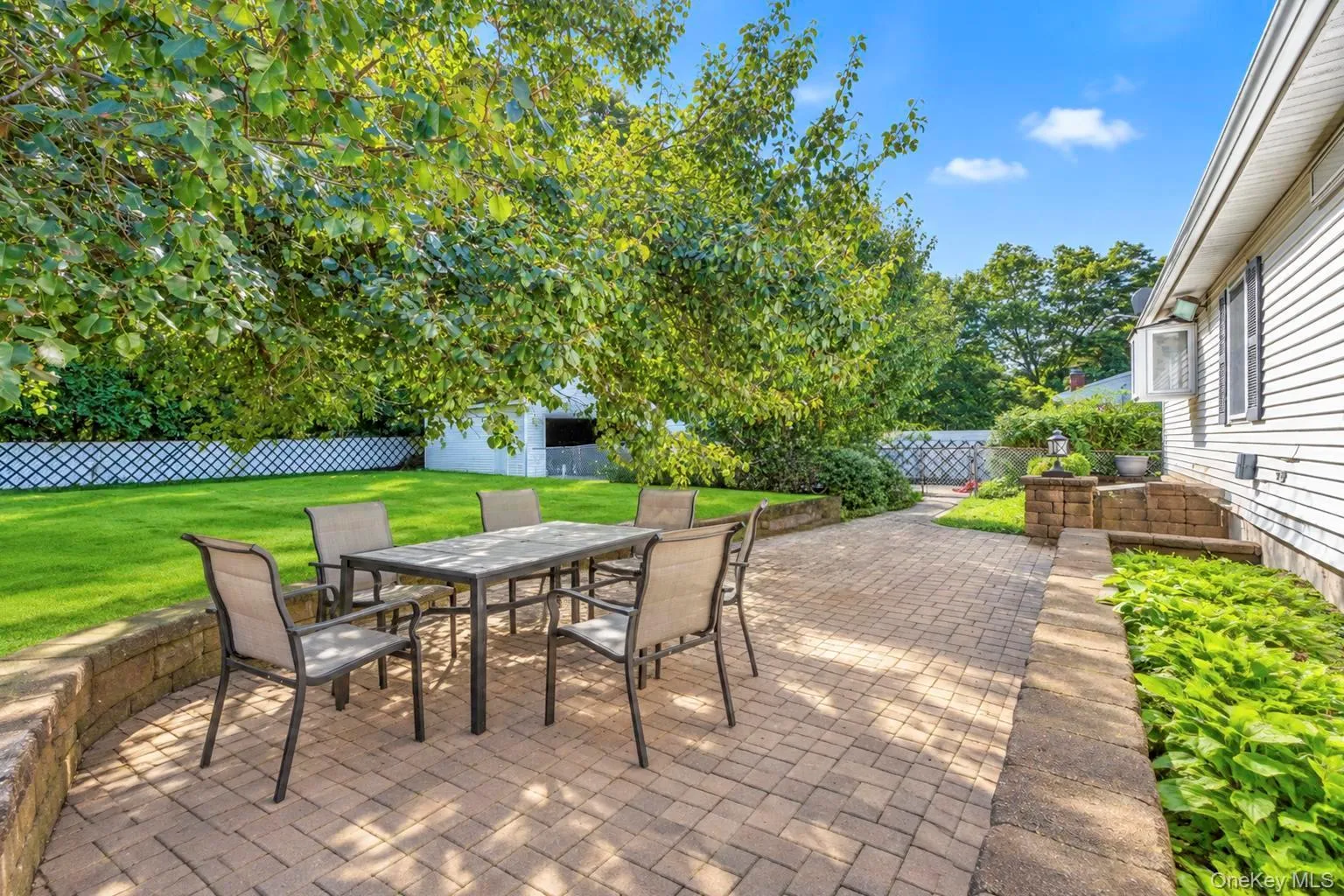 Expansive paver patio with a stone retaining wall, large lawn area, mature trees providing shade, and privacy fencing Expansive paver patio with a stone retaining wall, large lawn area, mature trees providing shade, and privacy fencing