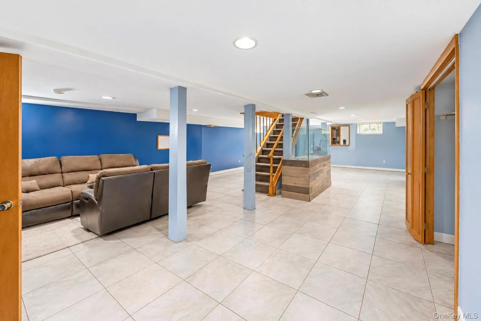 Spacious room featuring light-toned tile flooring, recessed lighting, wood-finish staircase, and built-in wood-finish cabinetry Spacious room featuring light-toned tile flooring, recessed lighting, wood-finish staircase, and built-in wood-finish cabinetry