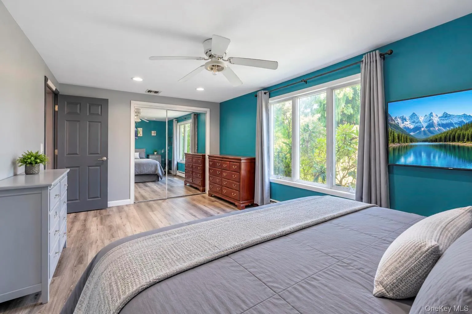 Expansive window with exterior landscaping, wood-finish flooring, ceiling fan, recessed lighting, and mirrored closet doors Expansive window with exterior landscaping, wood-finish flooring, ceiling fan, recessed lighting, and mirrored closet doors