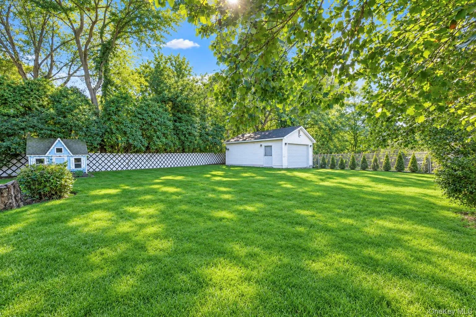 Expansive green lawn with a white lattice fence, mature trees, and a detached garage Expansive green lawn with a white lattice fence, mature trees, and a detached garage