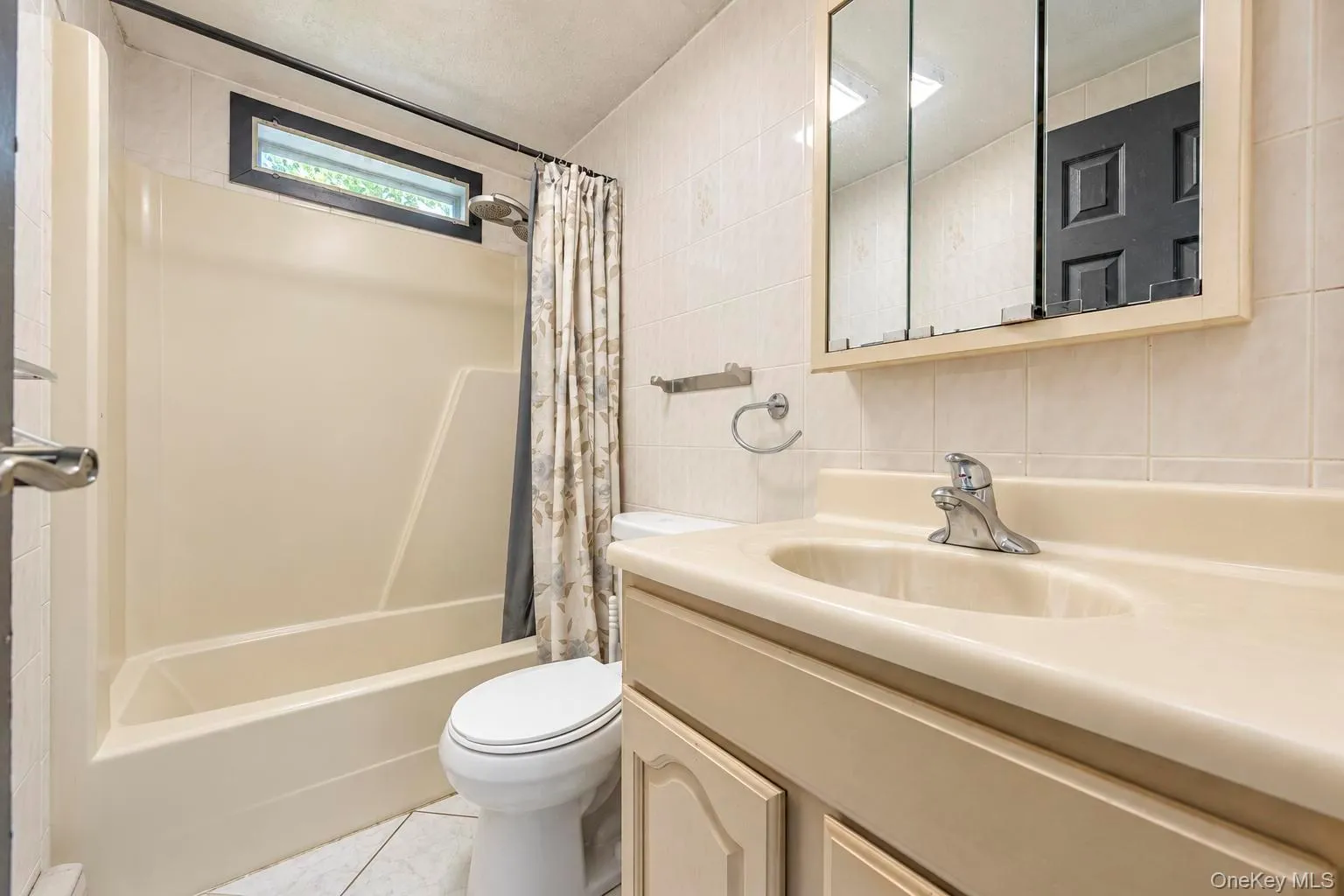 Tub-shower combination with a transom window, wall-mounted vanity with an integrated sink, tri-fold mirrored medicine cabinet, and tiled walls Tub-shower combination with a transom window, wall-mounted vanity with an integrated sink, tri-fold mirrored medicine cabinet, and tiled walls