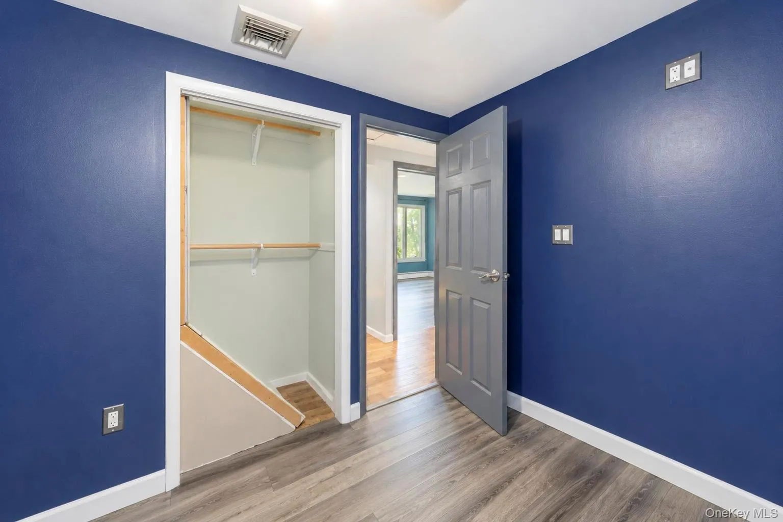 Wood-finish flooring with white trim, blue painted walls, and a closet with shelving Wood-finish flooring with white trim, blue painted walls, and a closet with shelving