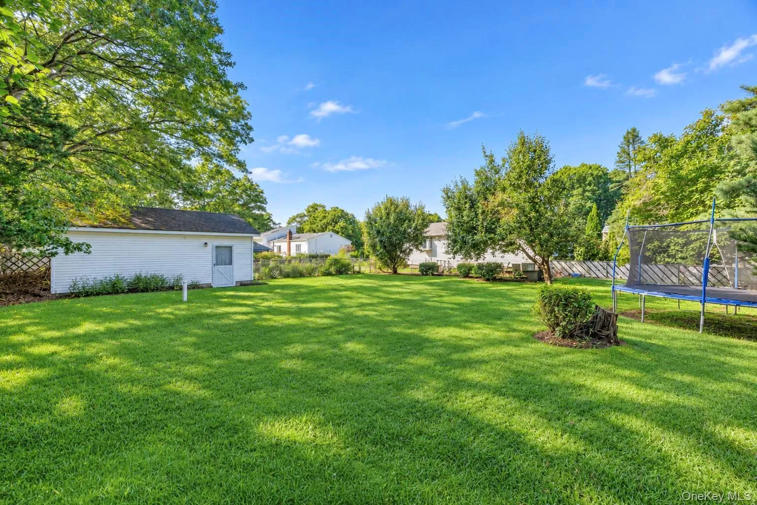 Expansive green lawn with mature trees and a detached white storage shed featuring a single door Expansive green lawn with mature trees and a detached white storage shed featuring a single door
