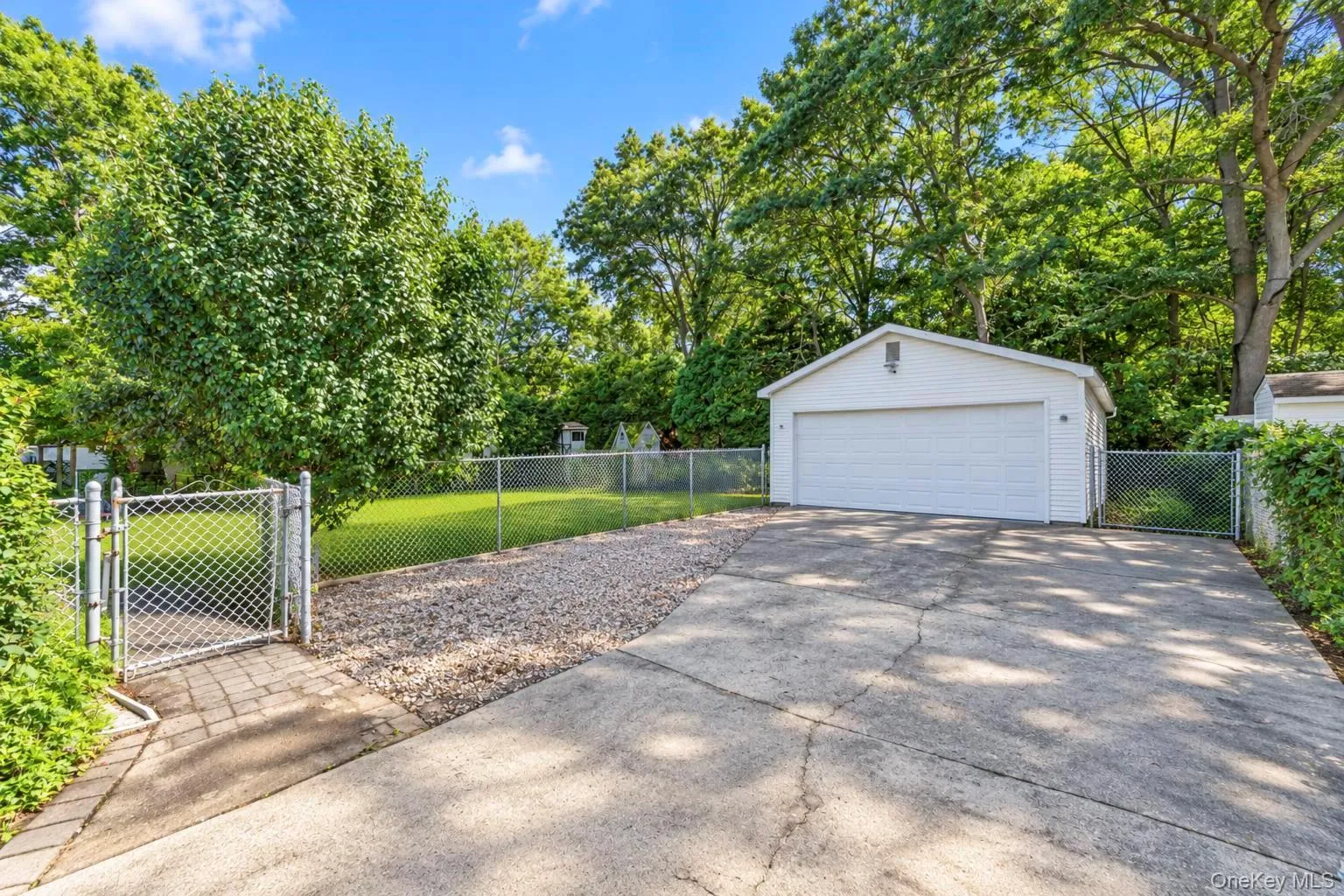 Detached two-car garage with white siding, concrete driveway, and chain-link fencing Detached two-car garage with white siding, concrete driveway, and chain-link fencing