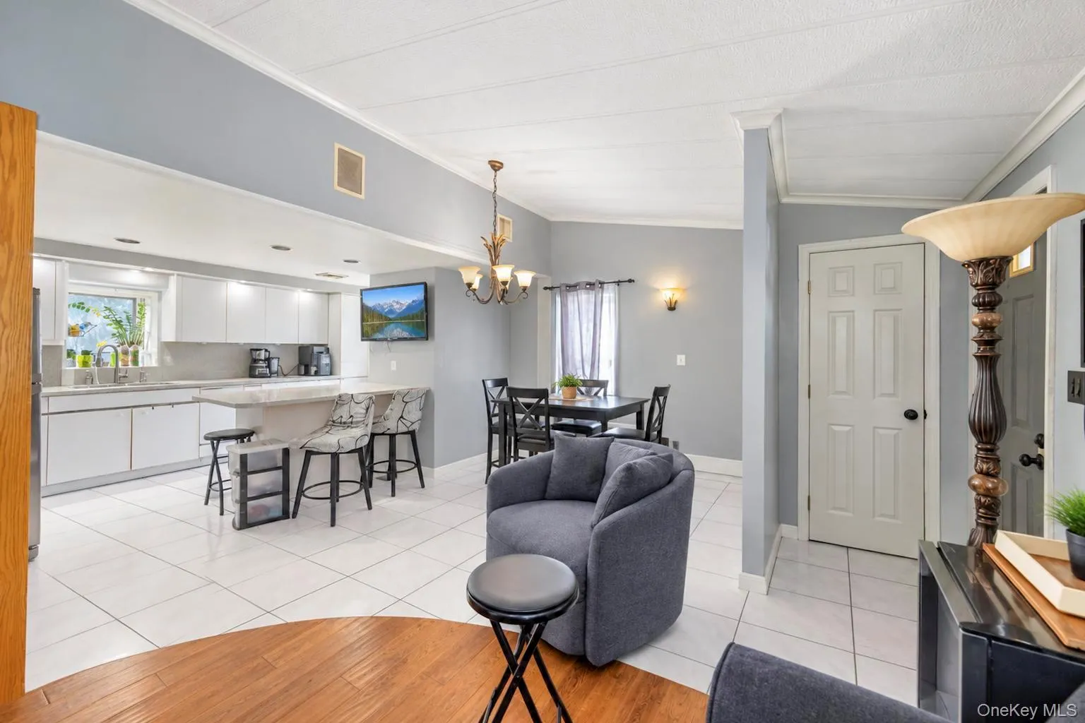 Open-concept living area featuring a kitchen with white cabinetry, a peninsula with seating, and white tile flooring Open-concept living area featuring a kitchen with white cabinetry, a peninsula with seating, and white tile flooring