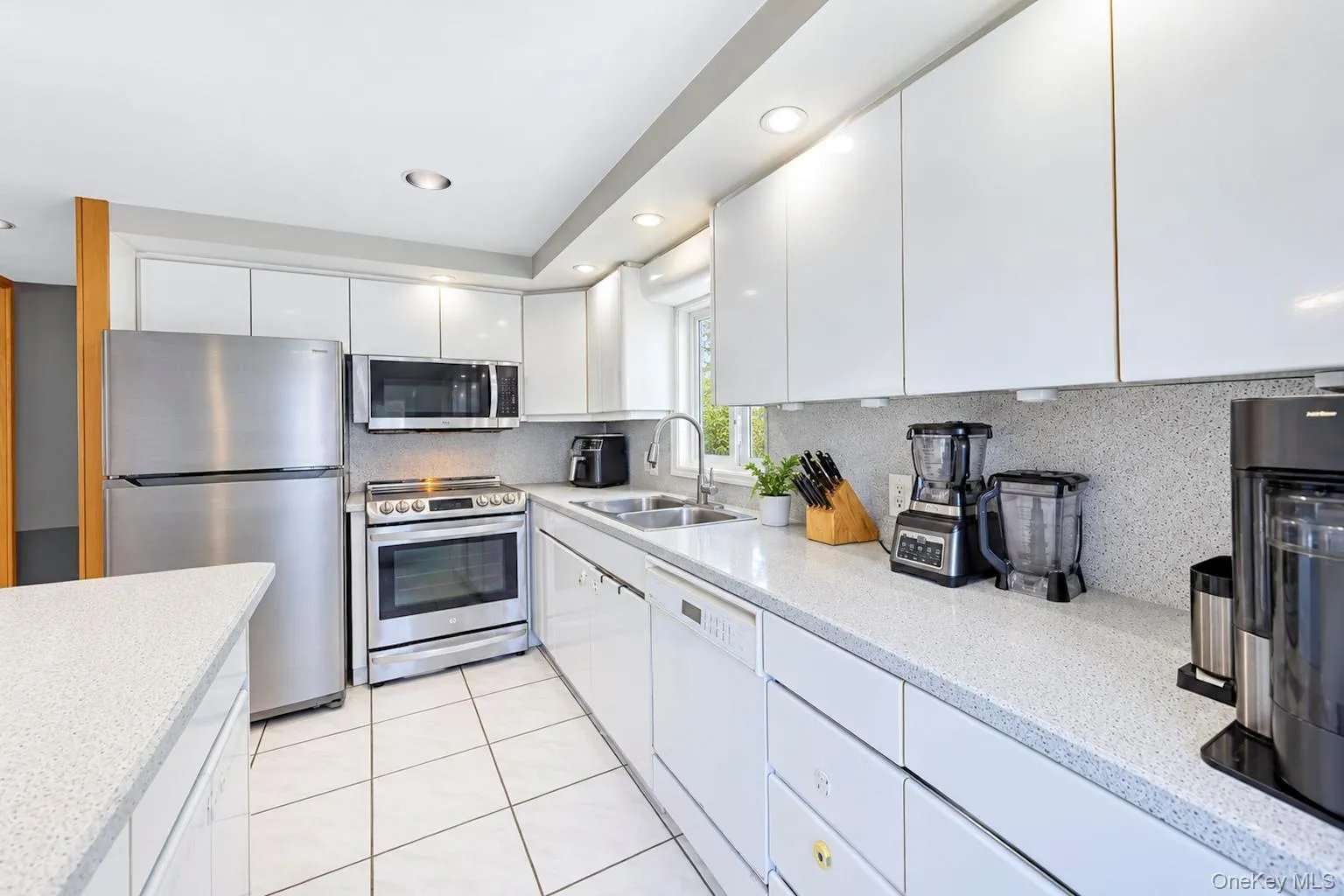 White flat-panel cabinetry, stainless steel appliances, white tile flooring, light-colored countertops, and recessed lighting White flat-panel cabinetry, stainless steel appliances, white tile flooring, light-colored countertops, and recessed lighting