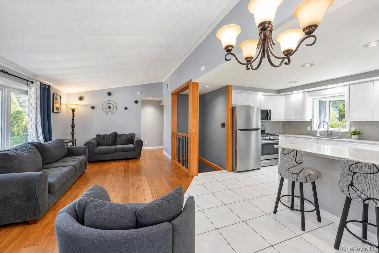 Open-concept living space featuring wood-finish flooring, a kitchen island with seating, stainless steel appliances, and white cabinetry Open-concept living space featuring wood-finish flooring, a kitchen island with seating, stainless steel appliances, and white cabinetry