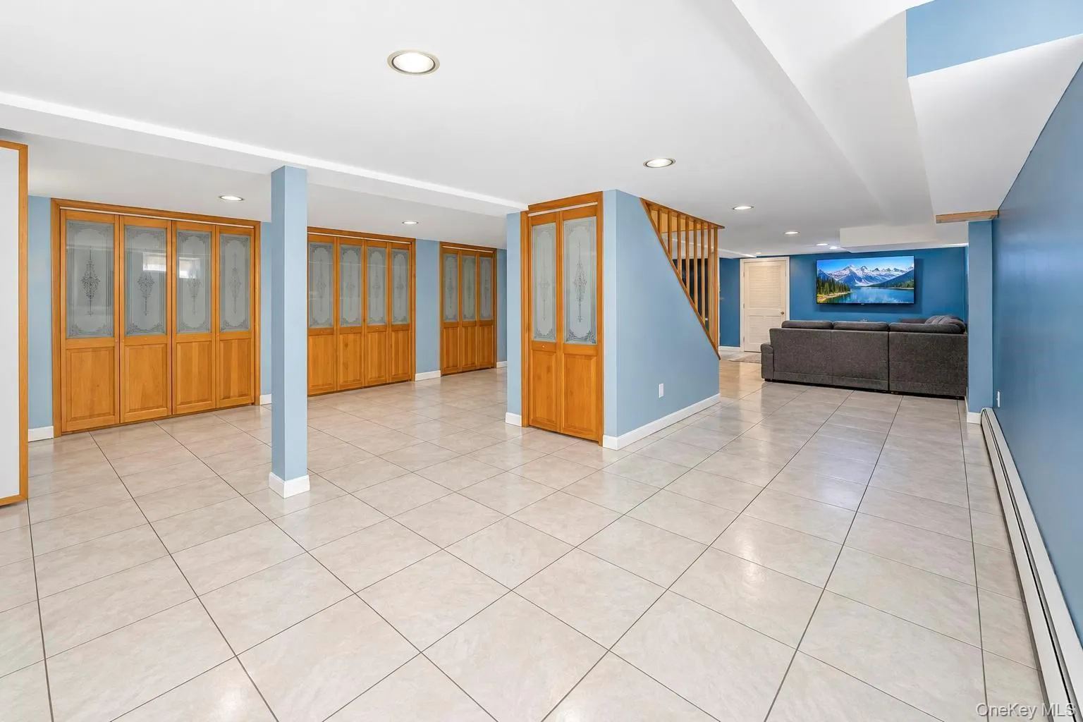 Spacious room featuring light-colored tile flooring, multiple built-in storage units with wood-finish doors and frosted glass panels, recessed ceiling lighting, and a painted blue accent wall Spacious room featuring light-colored tile flooring, multiple built-in storage units with wood-finish doors and frosted glass panels, recessed ceiling lighting, and a painted blue accent wall