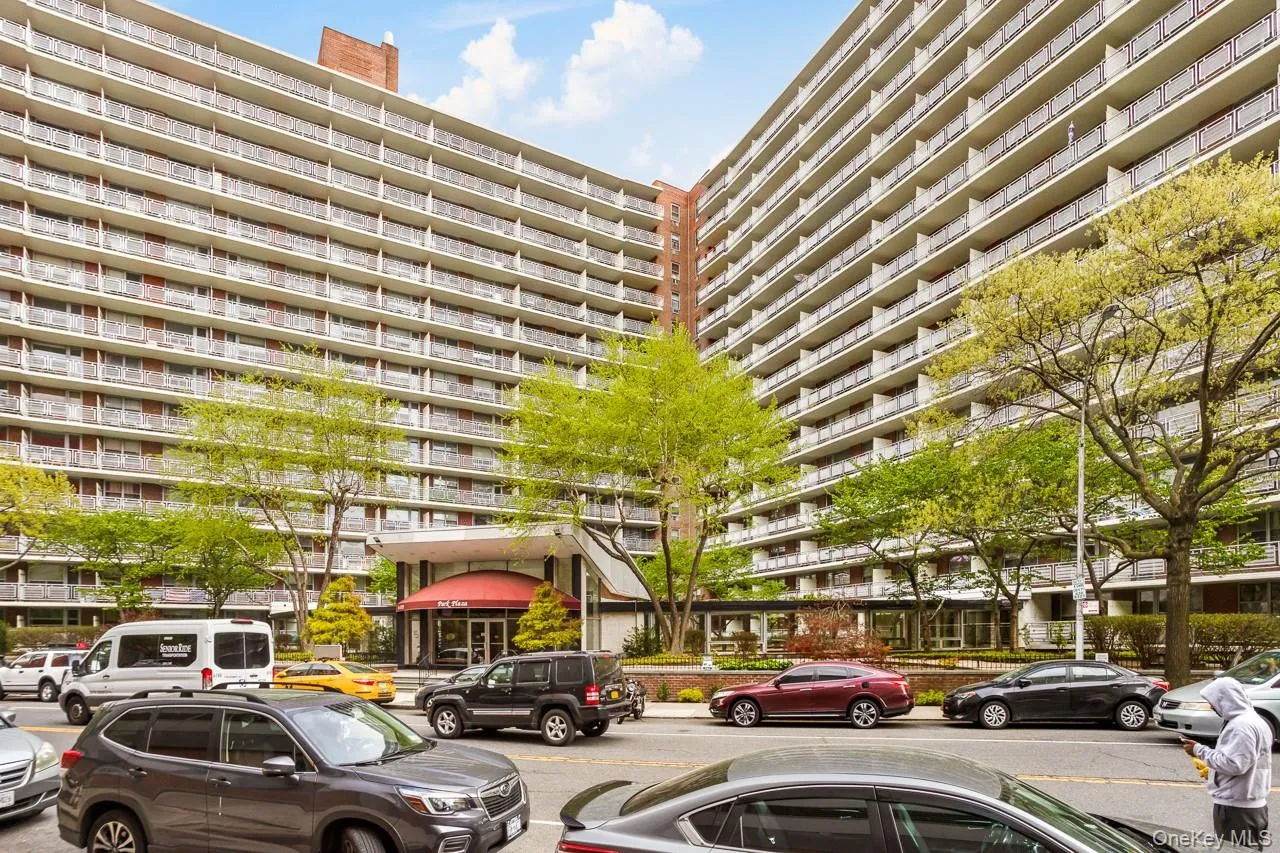 Multi-story building featuring numerous private balconies, a prominent red awning entrance, and established street-side trees Multi-story building featuring numerous private balconies, a prominent red awning entrance, and established street-side trees