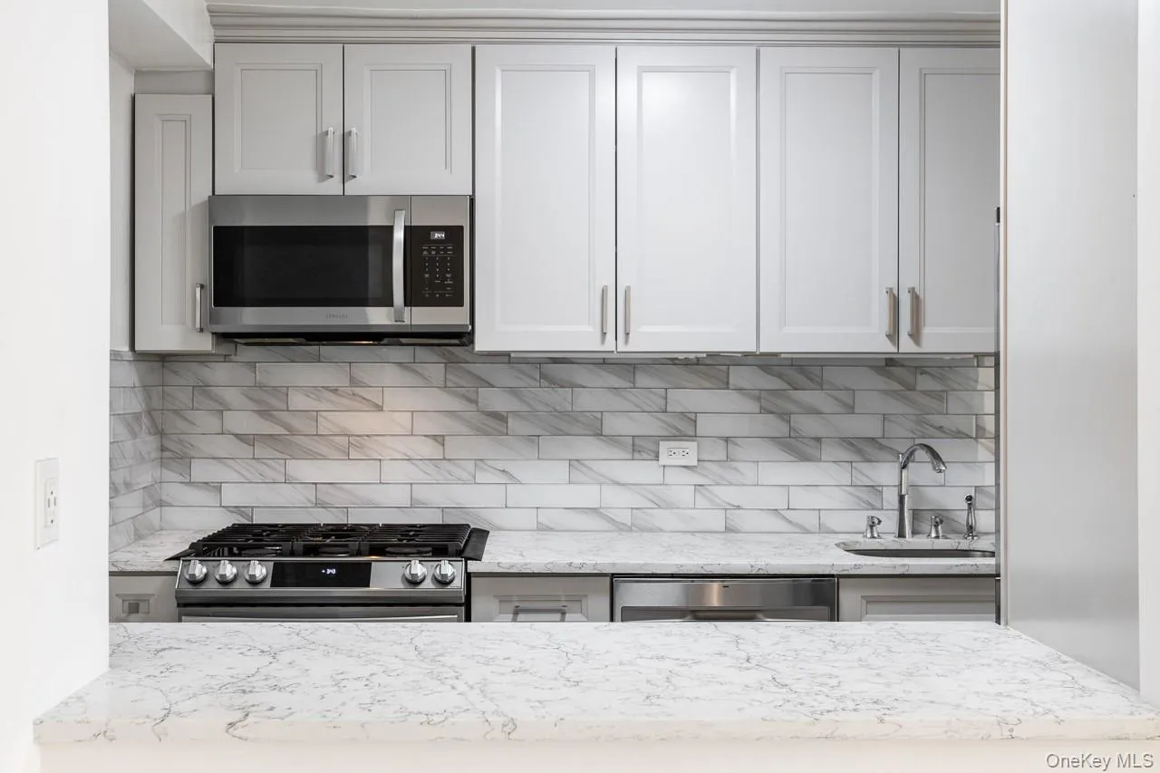 Light gray shaker-style cabinetry, stainless steel appliances, patterned tile backsplash, polished countertop, and an under-mount sink with a gooseneck faucet Light gray shaker-style cabinetry, stainless steel appliances, patterned tile backsplash, polished countertop, and an under-mount sink with a gooseneck faucet