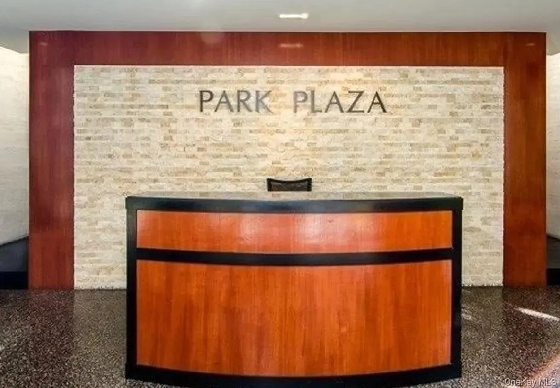 Curved wood reception desk, stone-finish accent wall, wood-paneled wall accents, recessed ceiling lighting, and polished stone flooring Curved wood reception desk, stone-finish accent wall, wood-paneled wall accents, recessed ceiling lighting, and polished stone flooring