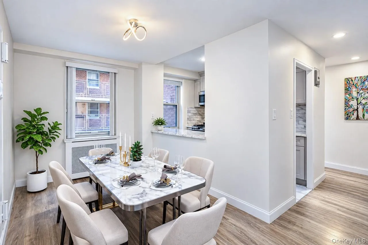 Open-concept dining area with wood-finish flooring, a contemporary ceiling fixture, and a built-in kitchen pass-through with a stone countertop Open-concept dining area with wood-finish flooring, a contemporary ceiling fixture, and a built-in kitchen pass-through with a stone countertop