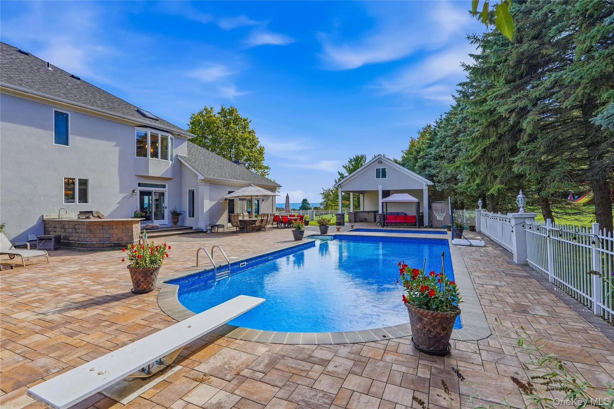 Expansive paver patio with an in-ground pool, diving board, and pool house Expansive paver patio with an in-ground pool, diving board, and pool house