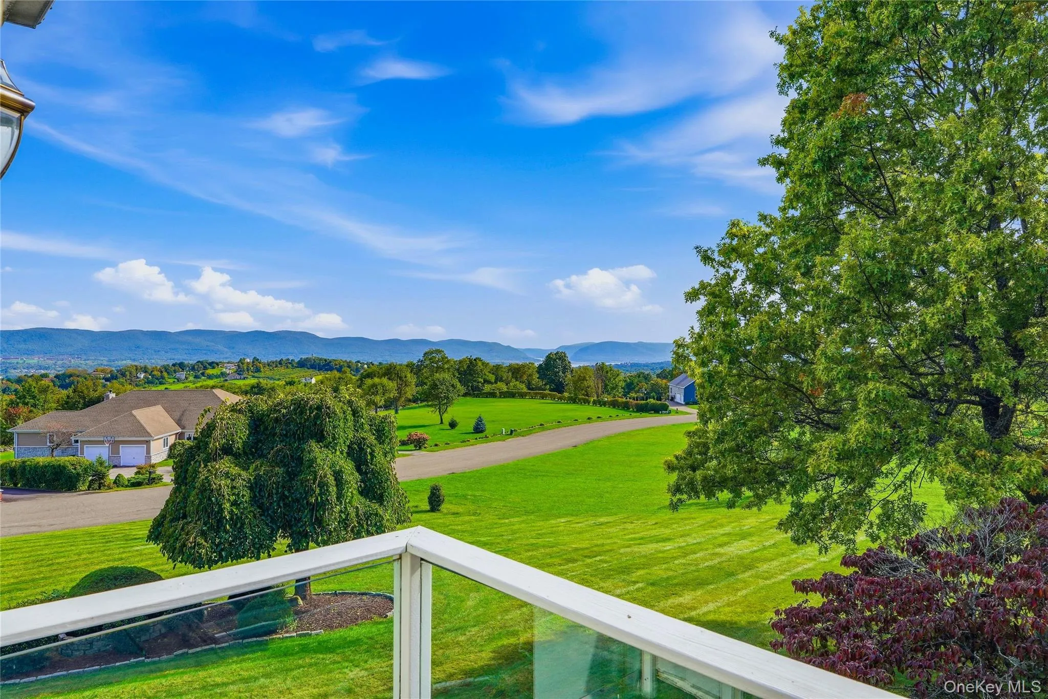 Balcony with glass railing, overlooking expansive landscape featuring rolling green hills, distant mountains, established trees, Hudson River views Balcony with glass railing, overlooking expansive landscape featuring rolling green hills, distant mountains, established trees, Hudson River views