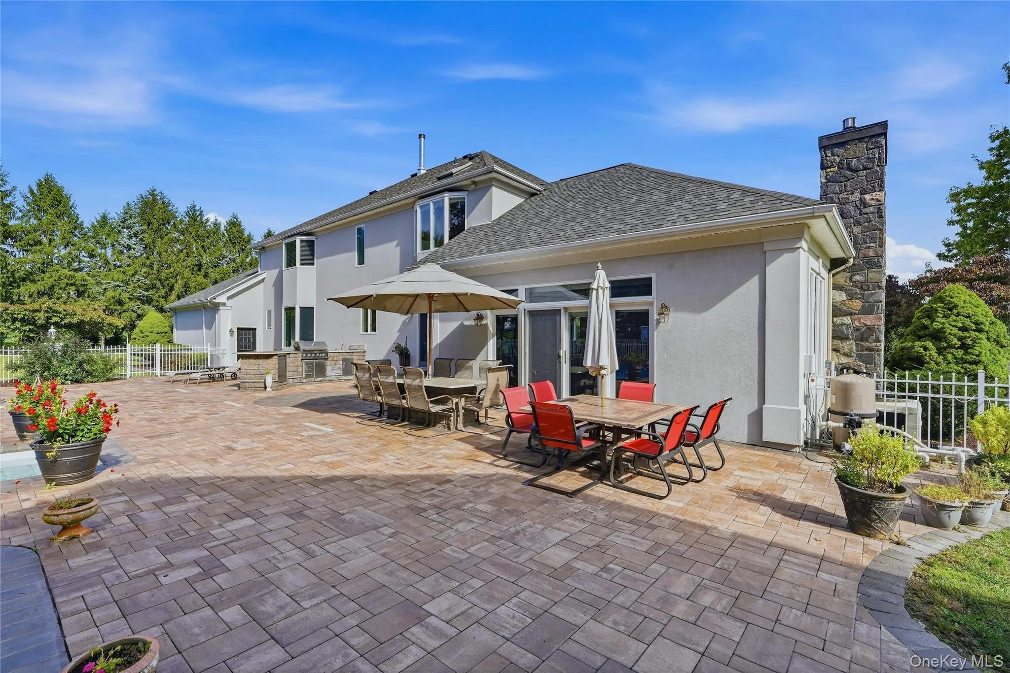 Expansive paver patio with a built-in outdoor kitchen, stone chimney, and stucco exterior Expansive paver patio with a built-in outdoor kitchen, stone chimney, and stucco exterior