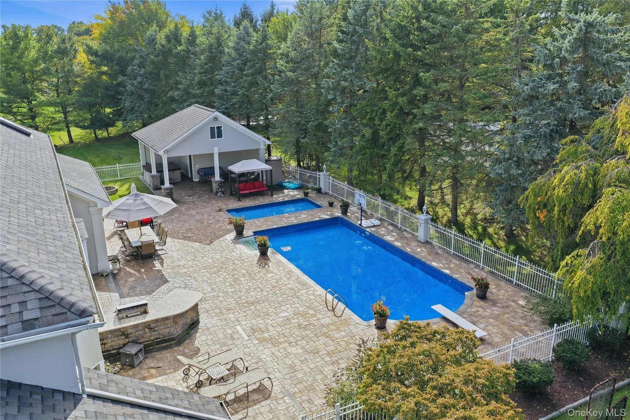 Expansive paver patio featuring a built-in outdoor kitchen, two swimming pools, and a pool house with covered outdoor space Expansive paver patio featuring a built-in outdoor kitchen, two swimming pools, and a pool house with covered outdoor space