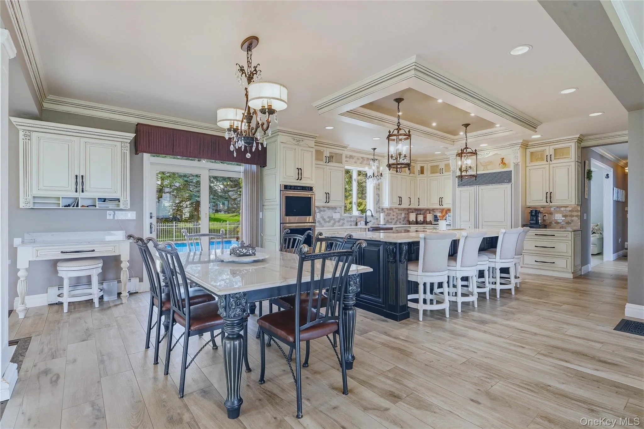 Wood-finish flooring, custom cabinetry, large kitchen island with seating, built-in appliances, quartzite table, and a sliding glass door Wood-finish flooring, custom cabinetry, large kitchen island with seating, built-in appliances, quartzite table, and a sliding glass door