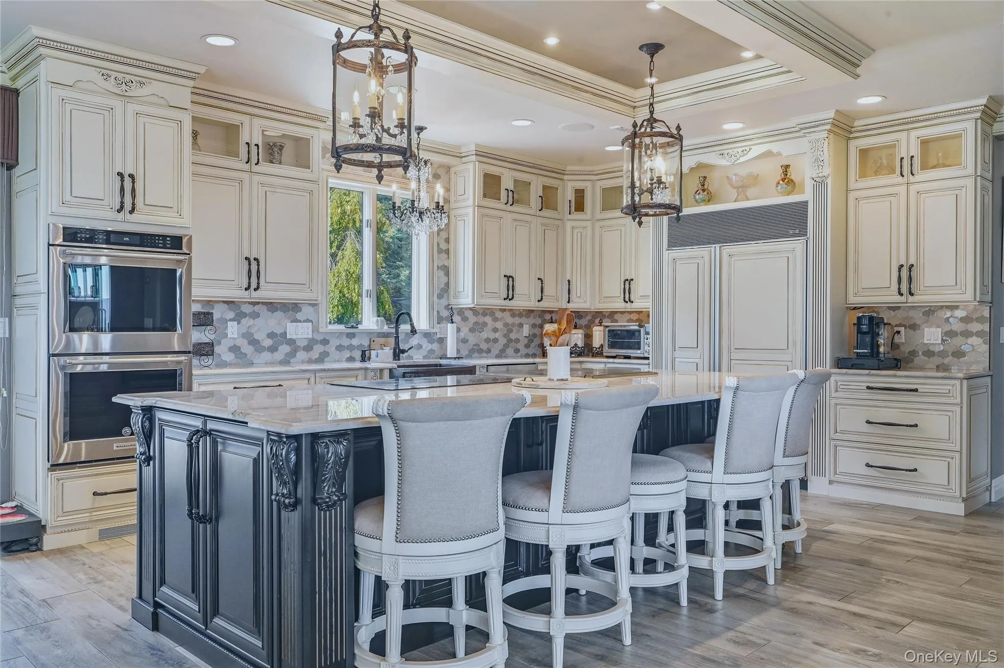 Gourmet kitchen featuring a large central island with seating, stainless steel built-in double ovens, extensive cabinetry, and a patterned marble backsplash Gourmet kitchen featuring a large central island with seating, stainless steel built-in double ovens, extensive cabinetry, and a patterned marble backsplash