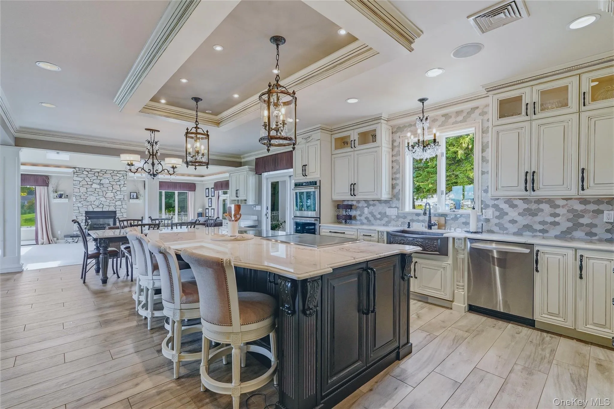 Gourmet kitchen featuring a large central island with seating, white shaker-style cabinetry, stainless steel appliances, and wood-look flooring Gourmet kitchen featuring a large central island with seating, white shaker-style cabinetry, stainless steel appliances, and wood-look flooring