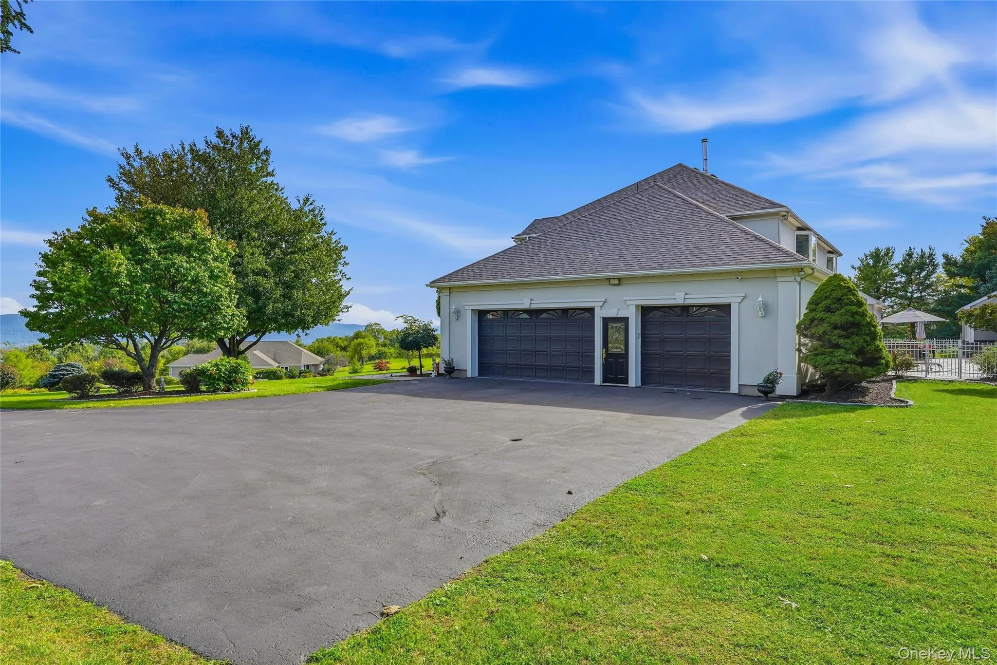 Three-car garage with black doors, paved driveway, expansive green lawn, mature trees, and a distant mountain backdrop Three-car garage with black doors, paved driveway, expansive green lawn, mature trees, and a distant mountain backdrop