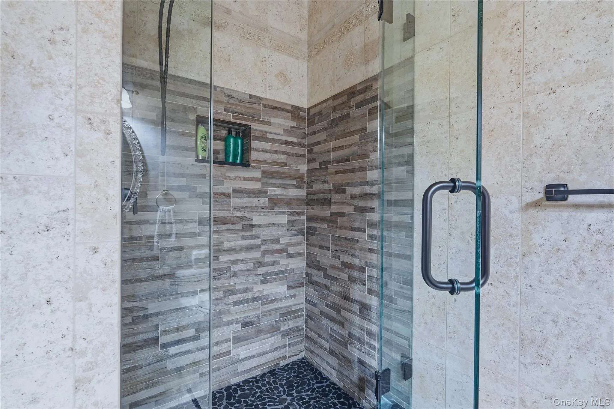 Glass-enclosed shower with a river rock floor, tiled walls, and a built-in shower niche Glass-enclosed shower with a river rock floor, tiled walls, and a built-in shower niche