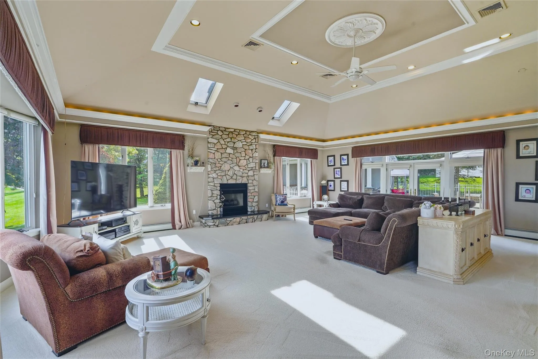 Vaulted ceiling with decorative medallion and ceiling fan, skylights, stone-clad fireplace, and expansive windows Vaulted ceiling with decorative medallion and ceiling fan, skylights, stone-clad fireplace, and expansive windows