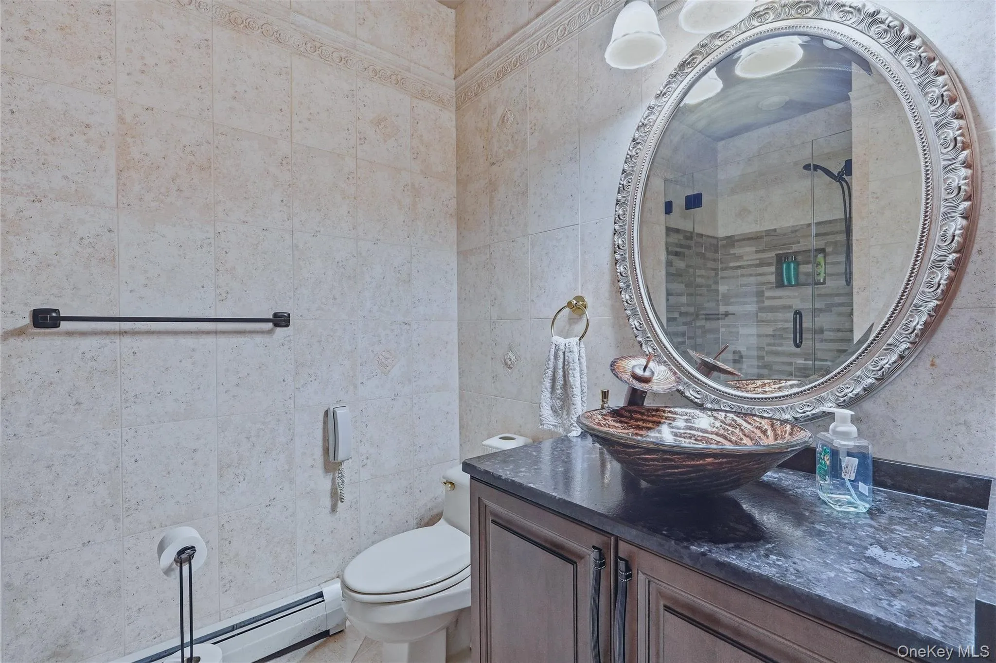 Custom vanity with a dark granite countertop and vessel sink, detailed ornate mirror, and tiled walls with decorative trim Custom vanity with a dark granite countertop and vessel sink, detailed ornate mirror, and tiled walls with decorative trim