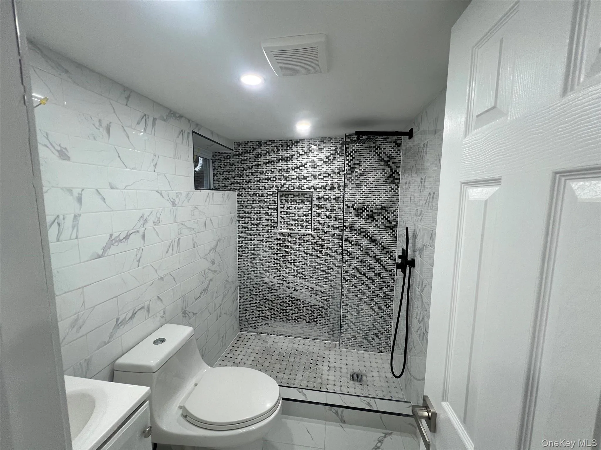 Bathroom featuring a glass-enclosed shower with mosaic tile, marble-look subway tile walls, a built-in shower niche, and a white vanity with an integrated sink Bathroom featuring a glass-enclosed shower with mosaic tile, marble-look subway tile walls, a built-in shower niche, and a white vanity with an integrated sink