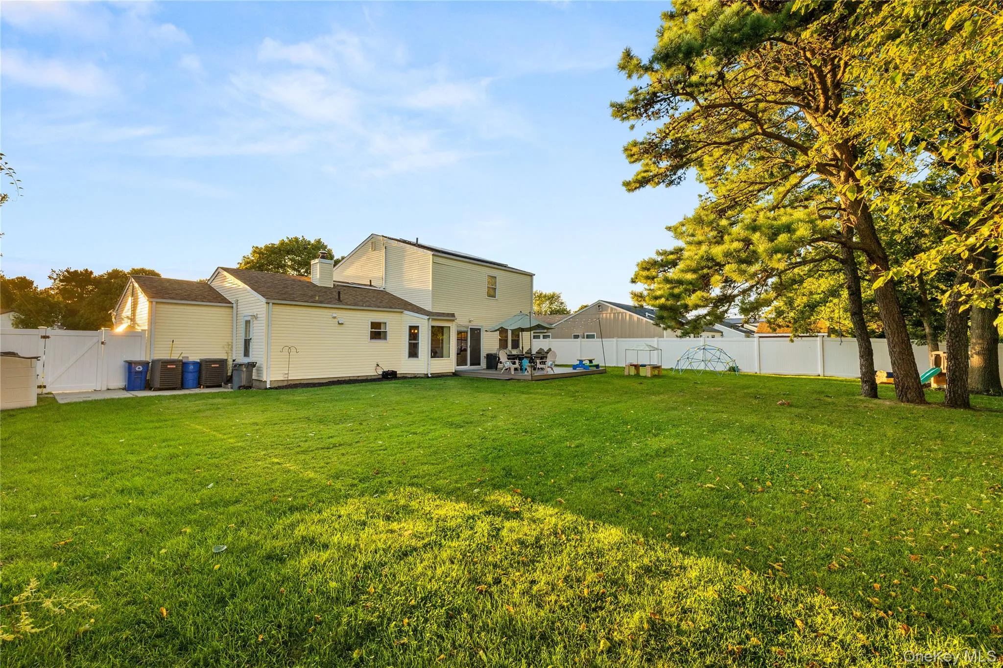 Expansive backyard featuring a manicured lawn, mature trees, and a white privacy fence Expansive backyard featuring a manicured lawn, mature trees, and a white privacy fence