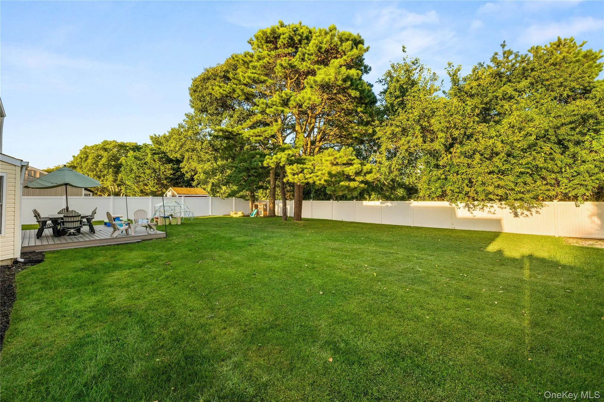 Expansive backyard featuring a manicured lawn, established trees, a raised deck, and a white privacy fence Expansive backyard featuring a manicured lawn, established trees, a raised deck, and a white privacy fence