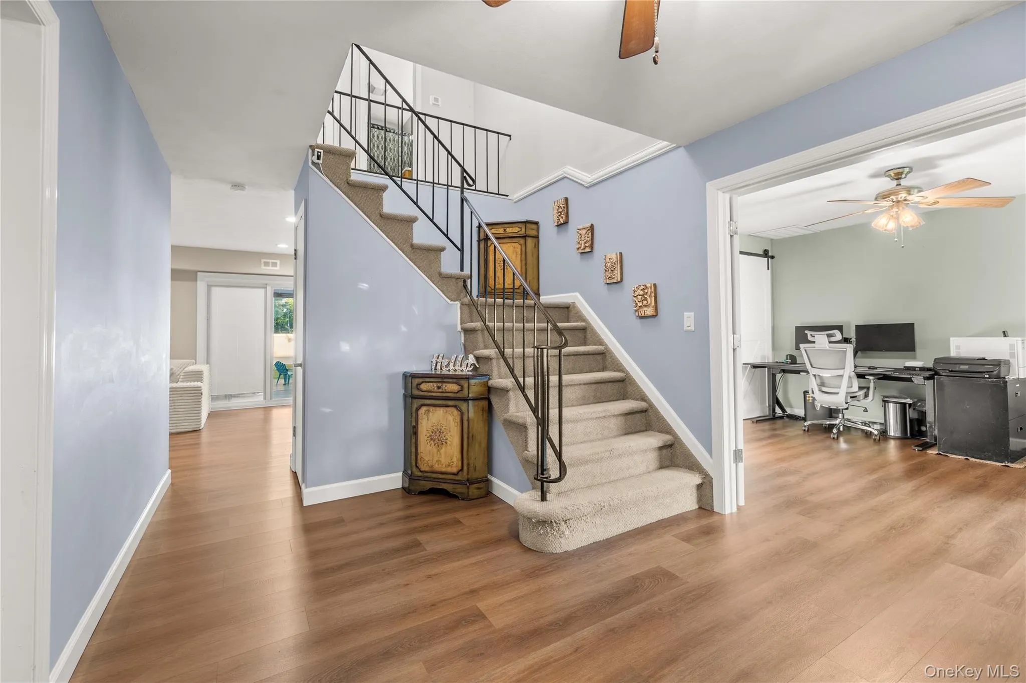 Wood-finish flooring, staircase with wrought iron railing, carpeted treads, and an open doorway leading to an additional room Wood-finish flooring, staircase with wrought iron railing, carpeted treads, and an open doorway leading to an additional room