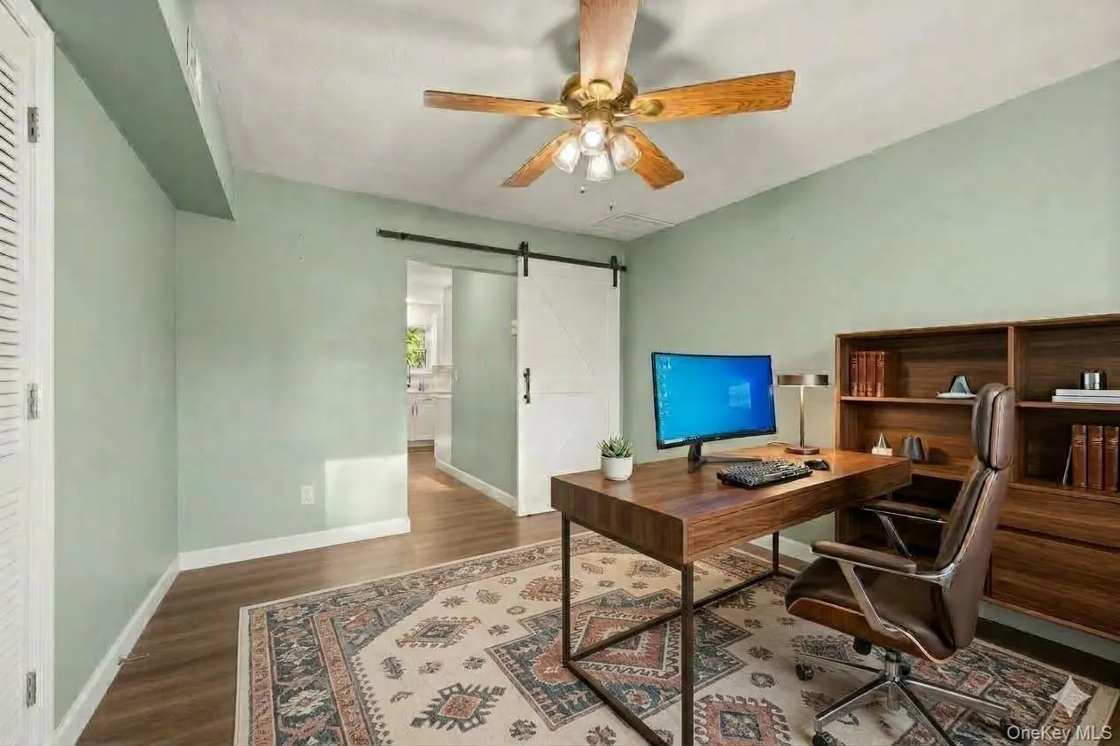Wood-finish flooring, ceiling fan, and a white barn door. AI edited, virtually staged. Wood-finish flooring, ceiling fan, and a white barn door. AI edited, virtually staged.