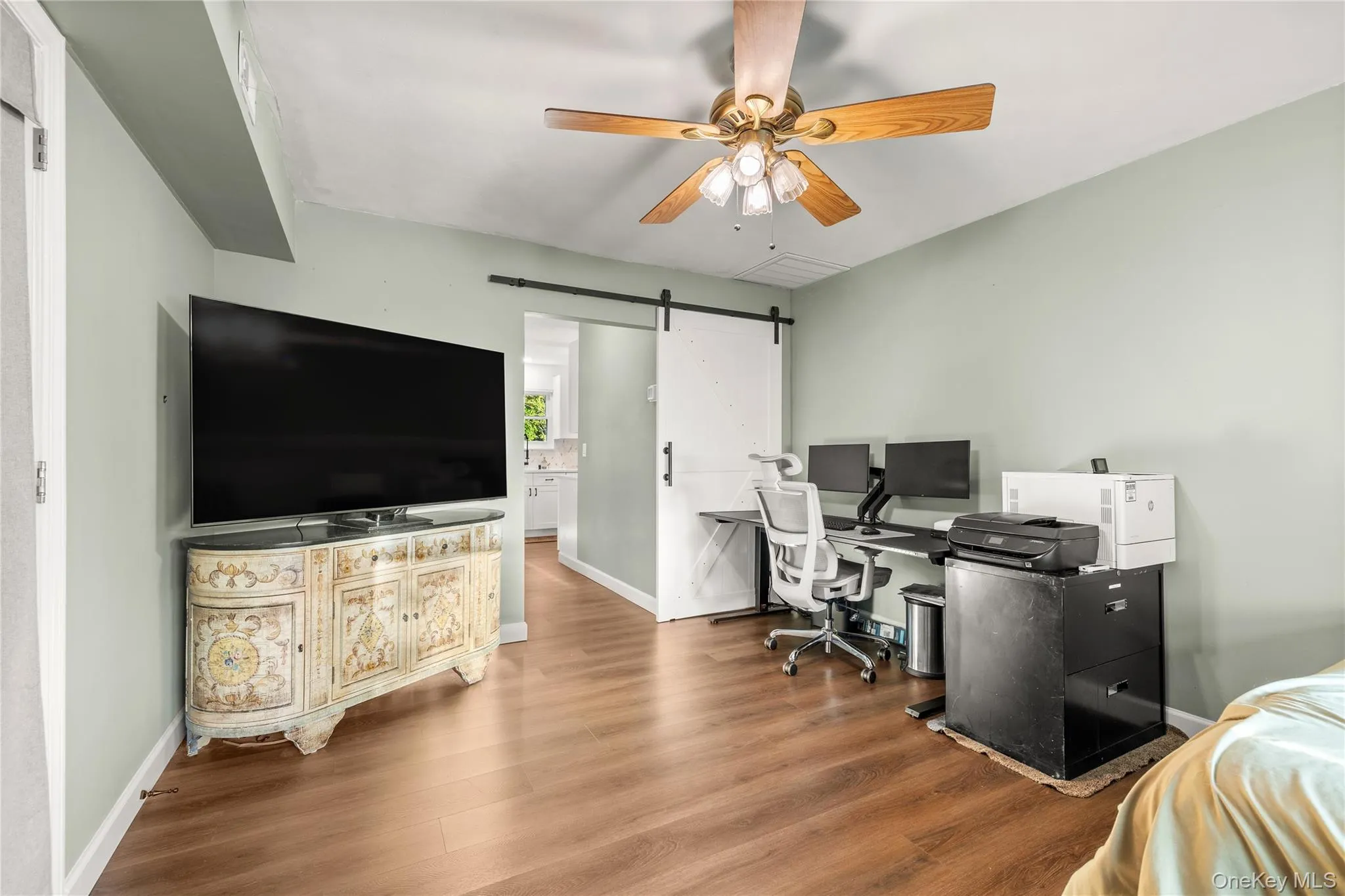 Bonus room on main level currently set up as an office space. Wood-finish flooring, ceiling fan with light fixture, and a white barn door Bonus room on main level currently set up as an office space. Wood-finish flooring, ceiling fan with light fixture, and a white barn door