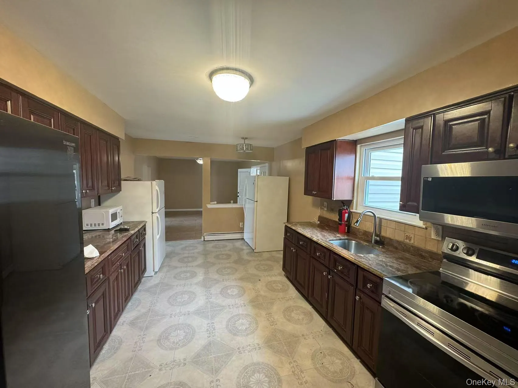 Kitchen featuring decorative backsplash, stainless steel appliances, dark brown cabinets, a sink, and a baseboard heating unit Kitchen featuring decorative backsplash, stainless steel appliances, dark brown cabinets, a sink, and a baseboard heating unit