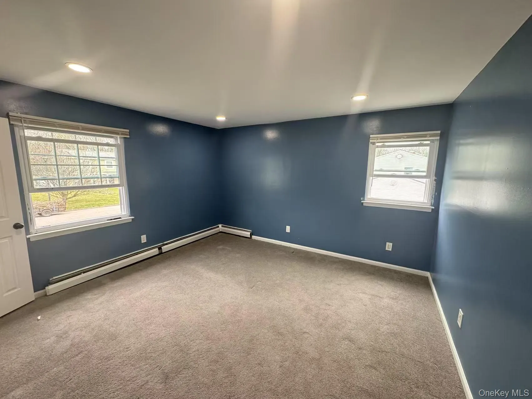 Empty room featuring baseboards, carpet flooring, plenty of natural light, and a baseboard radiator Empty room featuring baseboards, carpet flooring, plenty of natural light, and a baseboard radiator