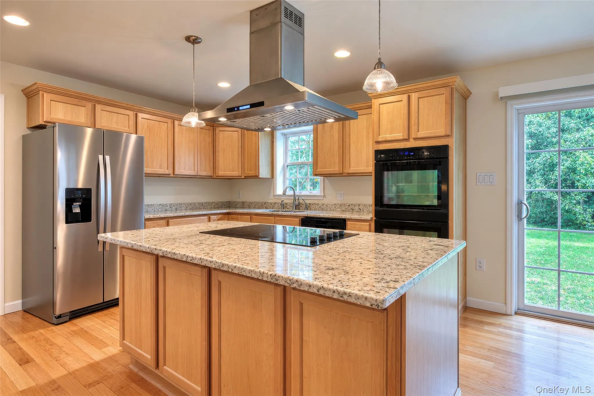 Kitchen featuring light wood cabinetry, granite countertops, stainless steel appliances, a center island with cooktop, and hardwood flooring Kitchen featuring light wood cabinetry, granite countertops, stainless steel appliances, a center island with cooktop, and hardwood flooring