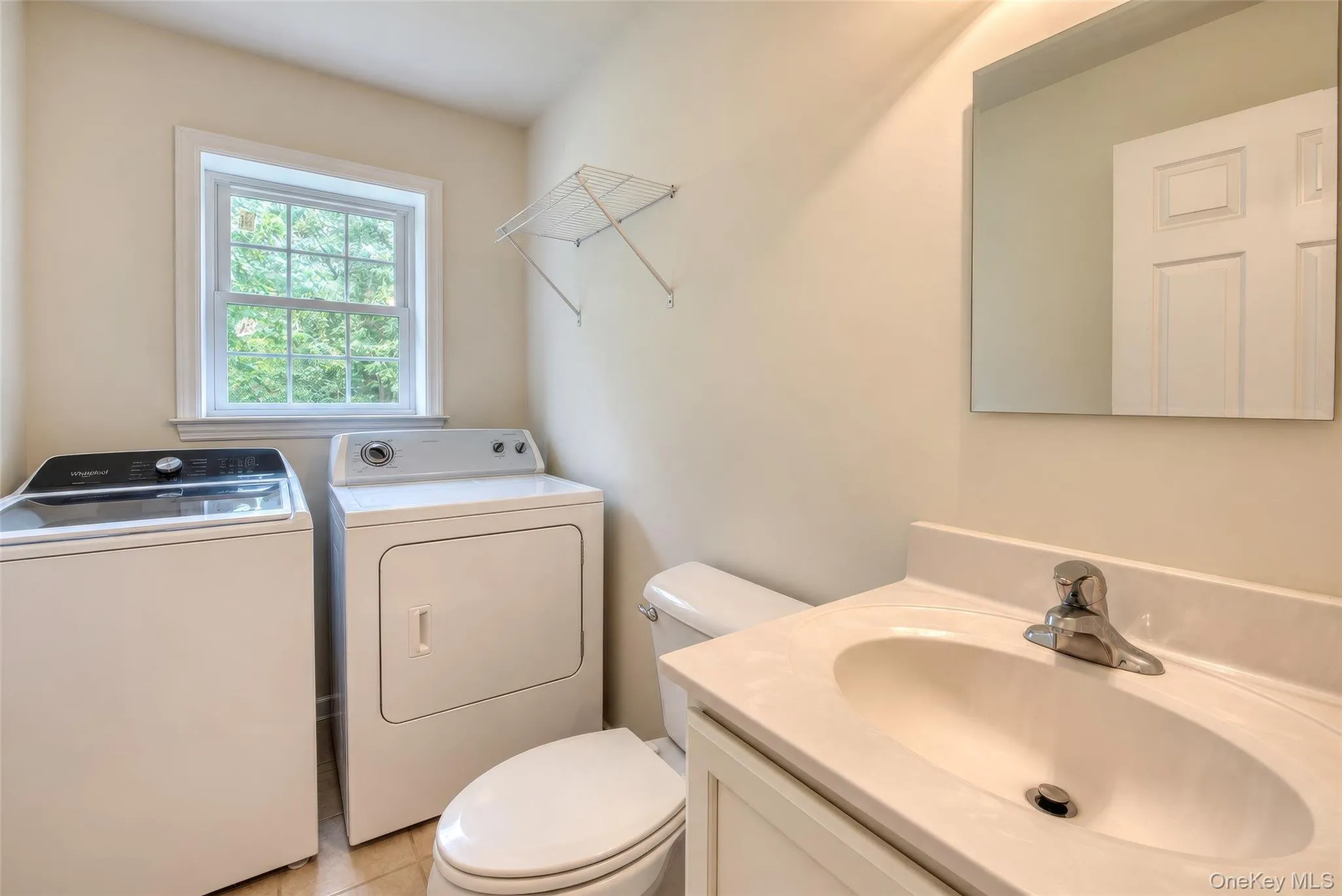 Laundry area with an operable window, built-in vanity with integrated sink, wall-mounted mirror, and tile flooring Laundry area with an operable window, built-in vanity with integrated sink, wall-mounted mirror, and tile flooring