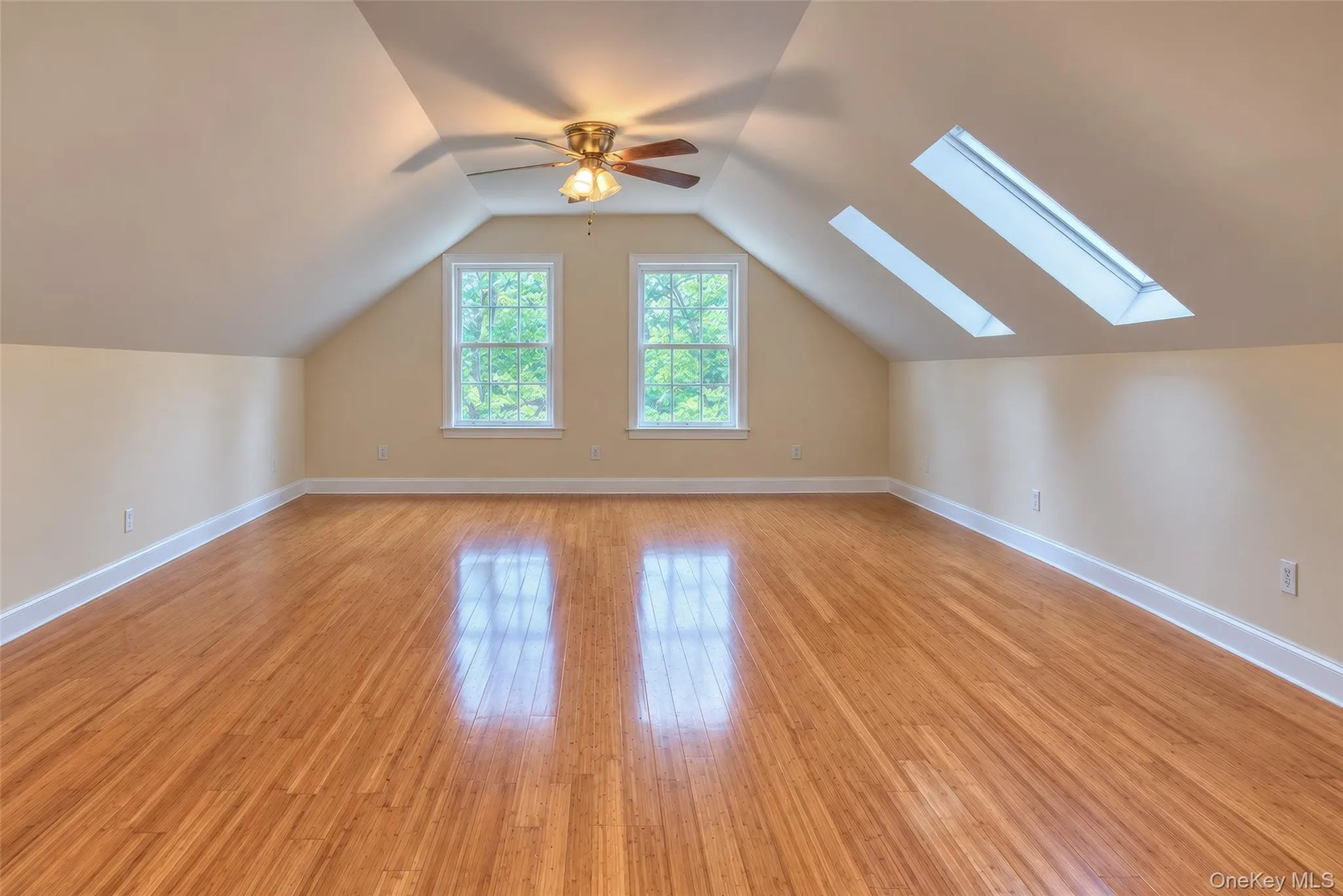 Bedroom featuring wood-finish flooring, two large skylights, two double-hung windows, a ceiling fan with integrated lighting, and sloped ceilings Bedroom featuring wood-finish flooring, two large skylights, two double-hung windows, a ceiling fan with integrated lighting, and sloped ceilings
