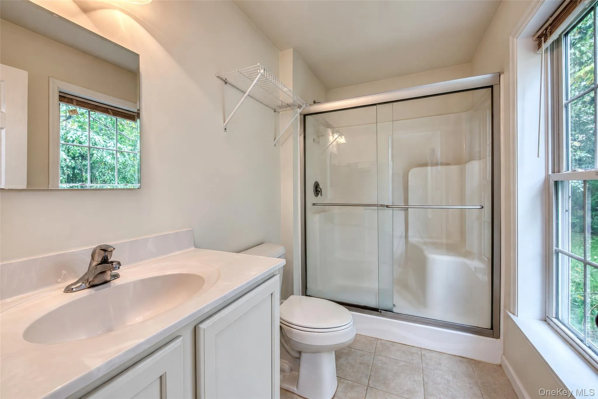 Bathroom featuring a vanity with an integrated sink, polished chrome faucet, a toilet, a shower with sliding glass doors, and a double-hung window Bathroom featuring a vanity with an integrated sink, polished chrome faucet, a toilet, a shower with sliding glass doors, and a double-hung window