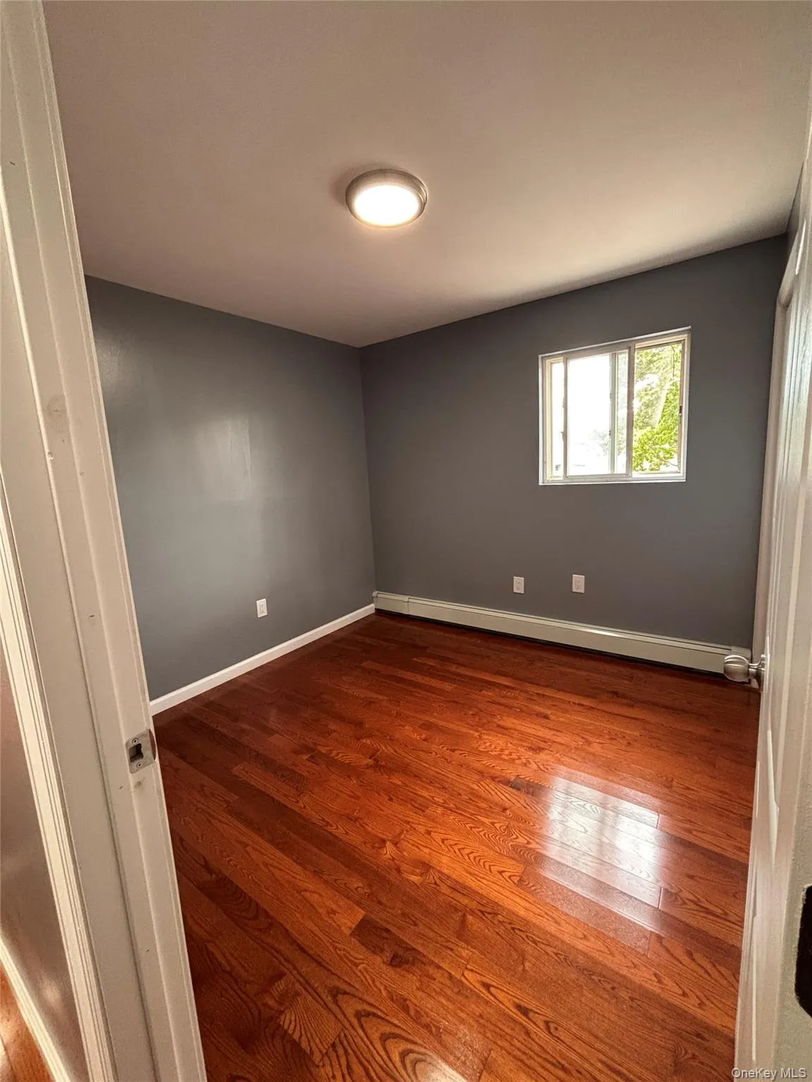 Hardwood flooring, painted walls, window with trim, and a ceiling-mounted light fixture Hardwood flooring, painted walls, window with trim, and a ceiling-mounted light fixture