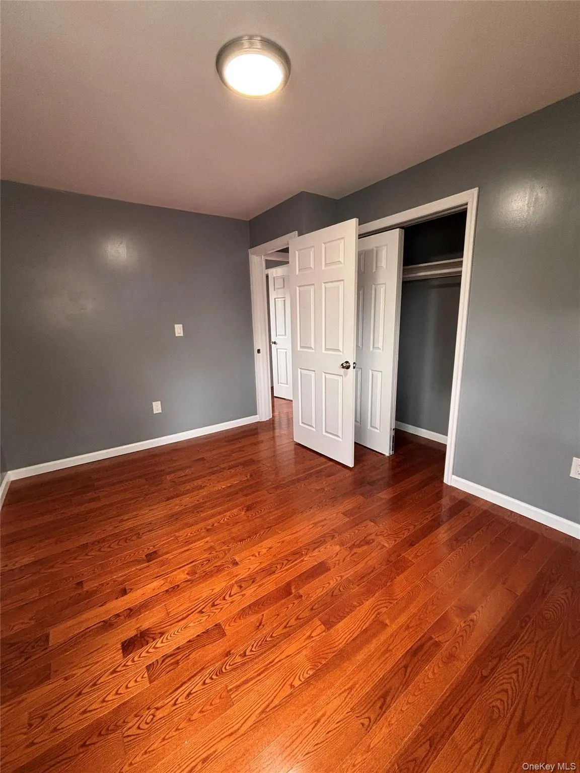 Hardwood flooring, painted walls, white trim, flush mount ceiling light, and bi-fold closet doors Hardwood flooring, painted walls, white trim, flush mount ceiling light, and bi-fold closet doors