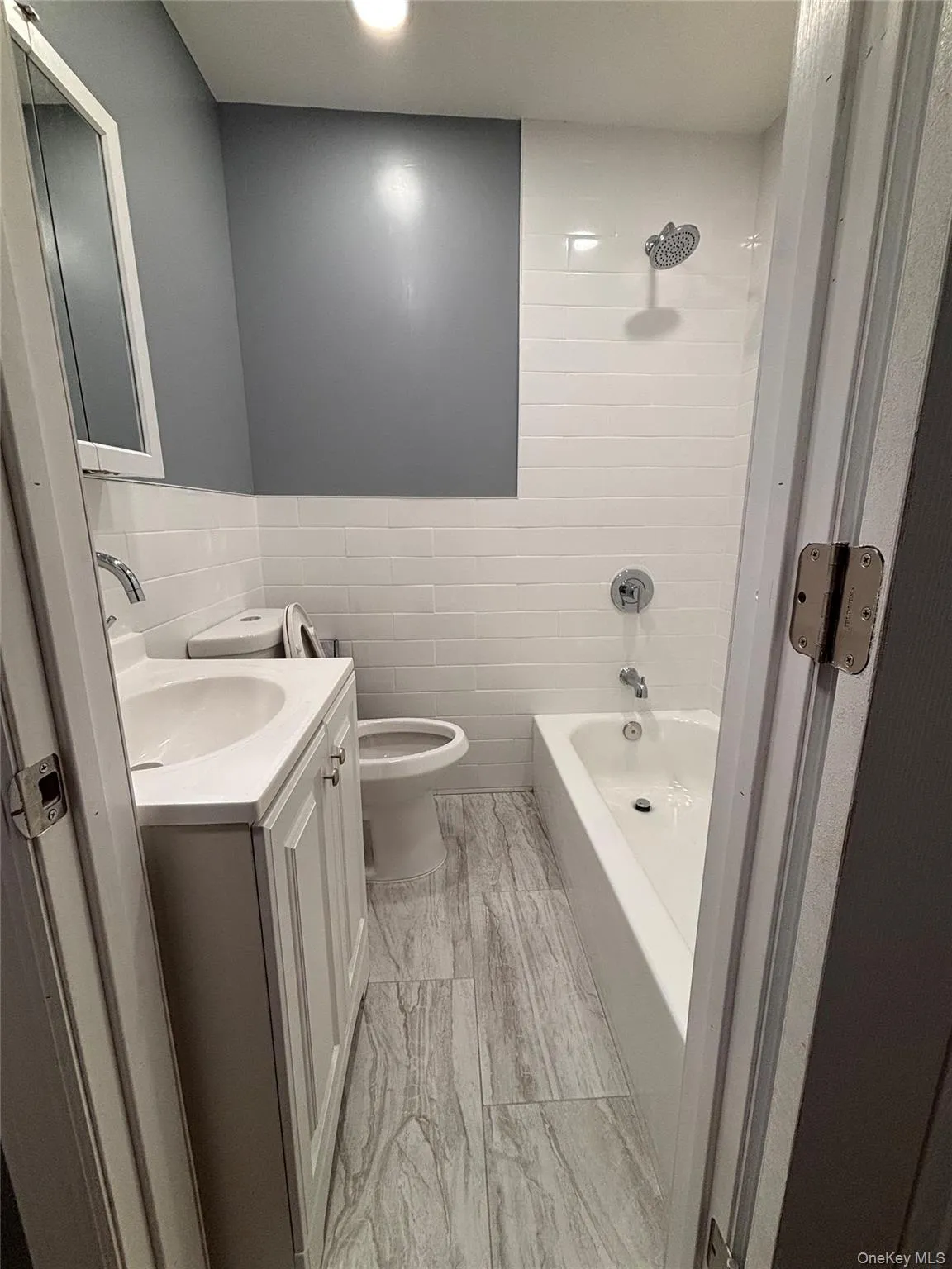 White subway tile shower surround, a built-in bathtub, a white vanity with an integrated sink, and wood-finish tile flooring White subway tile shower surround, a built-in bathtub, a white vanity with an integrated sink, and wood-finish tile flooring
